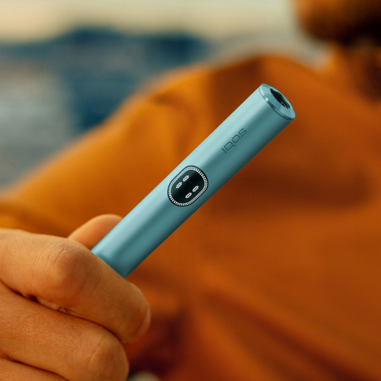 A hand holding an IQOS ILUMA i holder in Breeze Blue color.