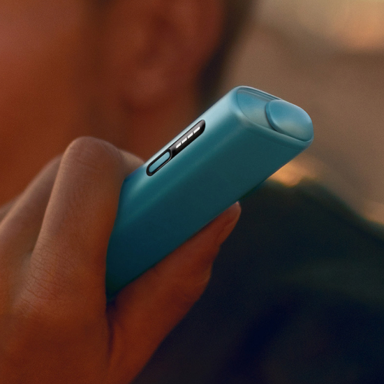 A hand holding an IQOS ILUMA i ONE device in Breeze Blue color.