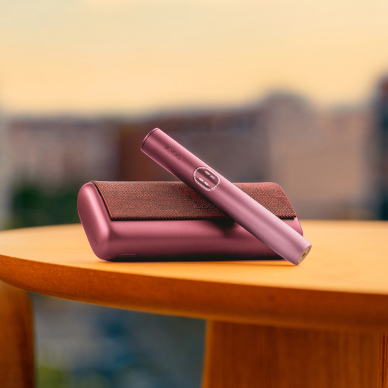 IQOS ILUMA i PRIME device in Garnet red color laying on a wooden table.