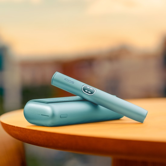 IQOS ILUMA i PRIME device in Breeze Blue color laying on a wooden table.