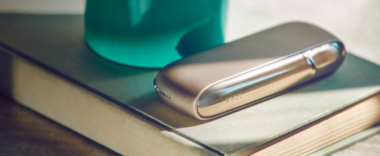 Brilliant gold IQOS 3 DUO on a book against a green background