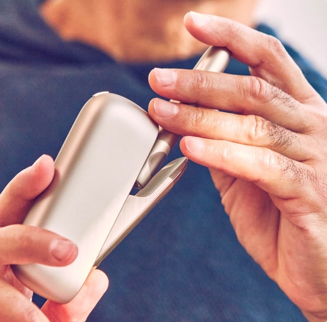 Hands holding an IQOS device.