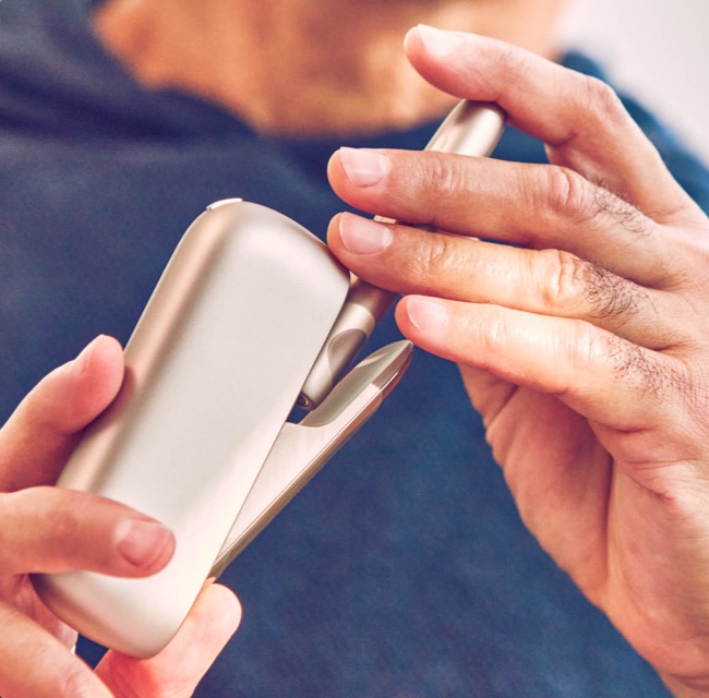 Hands holding an IQOS device.
