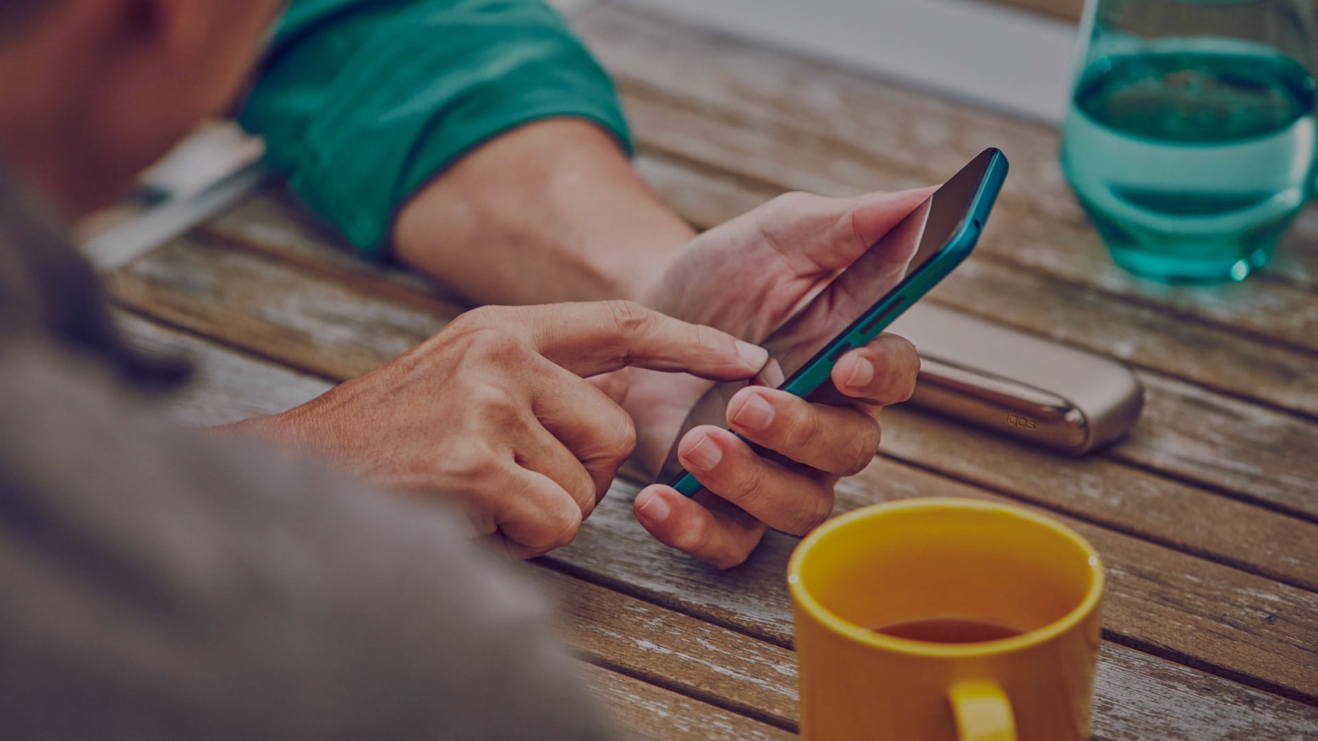 Man checking his phone with the IQOS device on the table