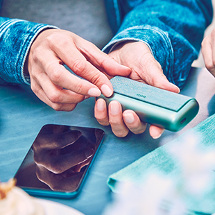 Man checking his phone with the IQOS device on the table